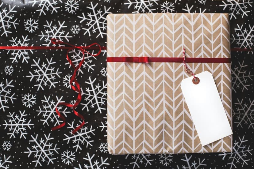 Brown chevron gift box tied with a red ribbon and white tag centered on a black snowflake-patterned background.