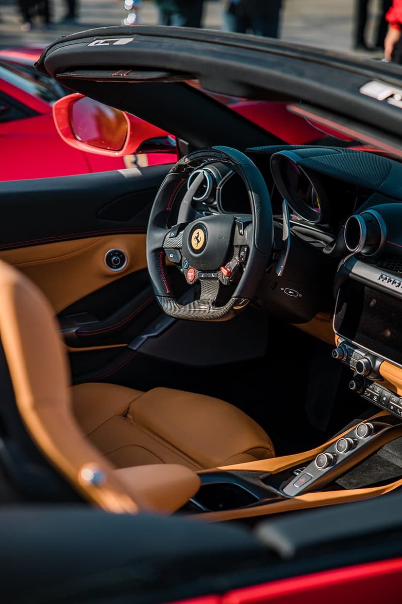 Ferrari steering wheel with a prancing horse emblem near tan leather seats and a carbon fiber dashboard.