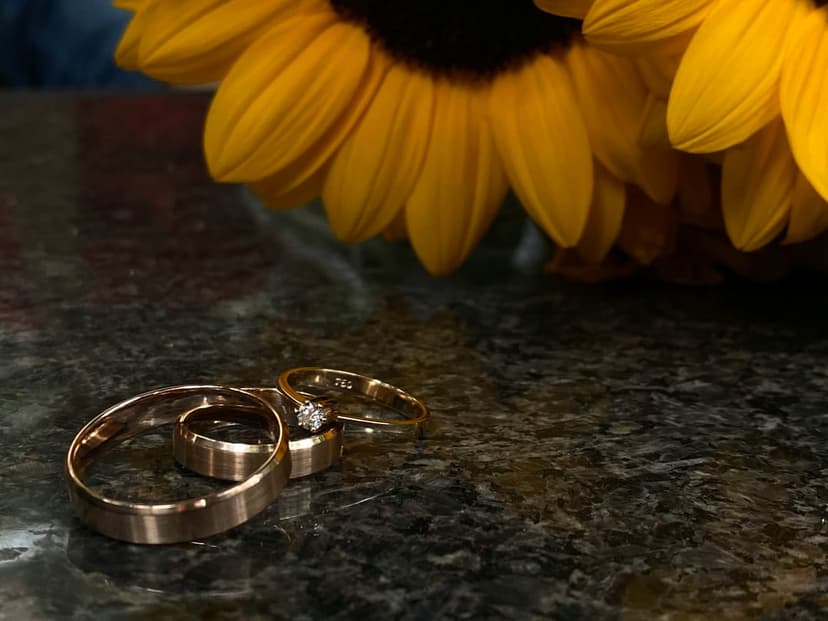 Two gold wedding rings with a diamond rest on dark marble against a background of soft yellow sunflower petals.