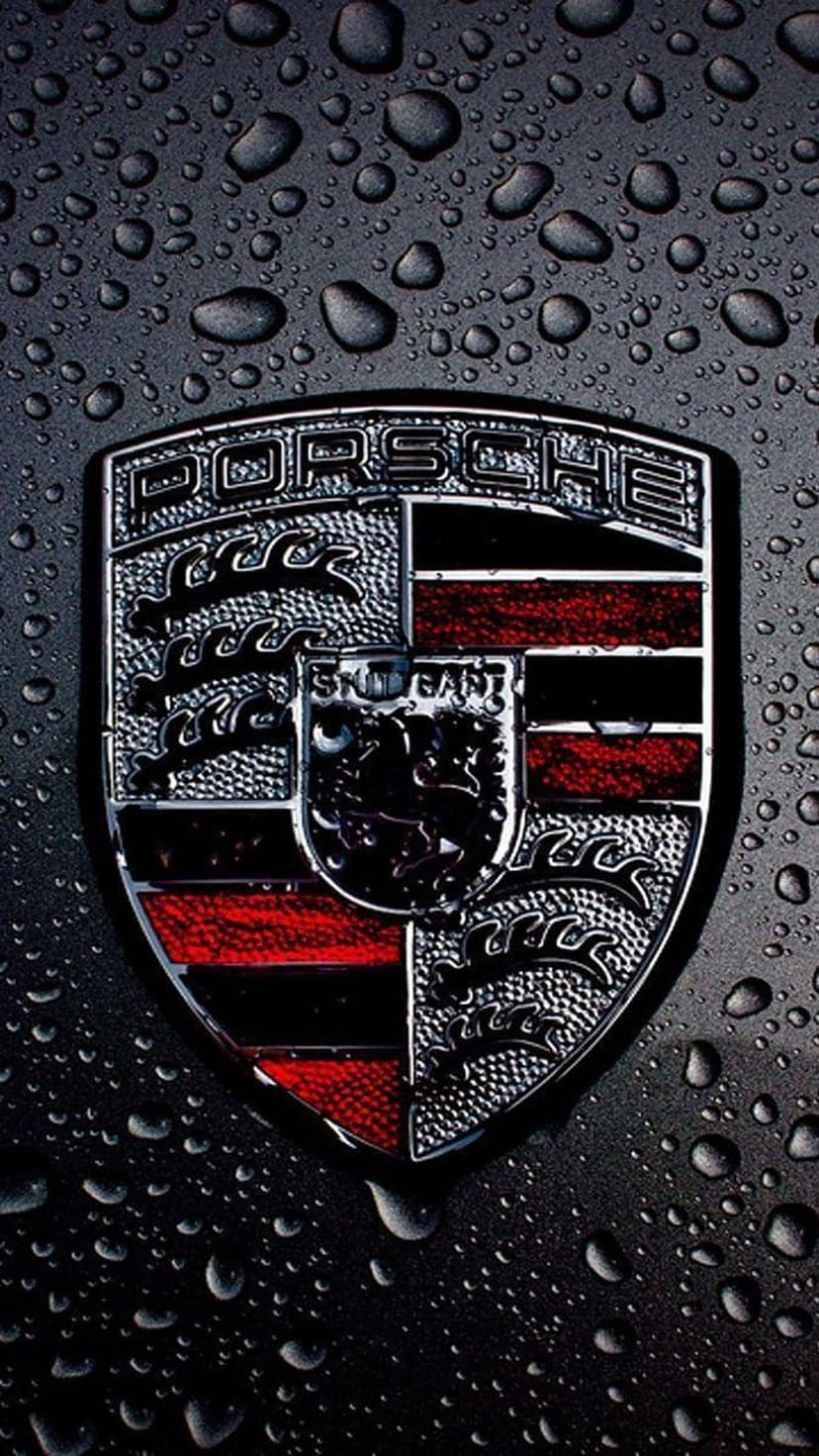 Porsche crest badge with water droplets on a dark textured surface, highlighting gold and red enamel details.
