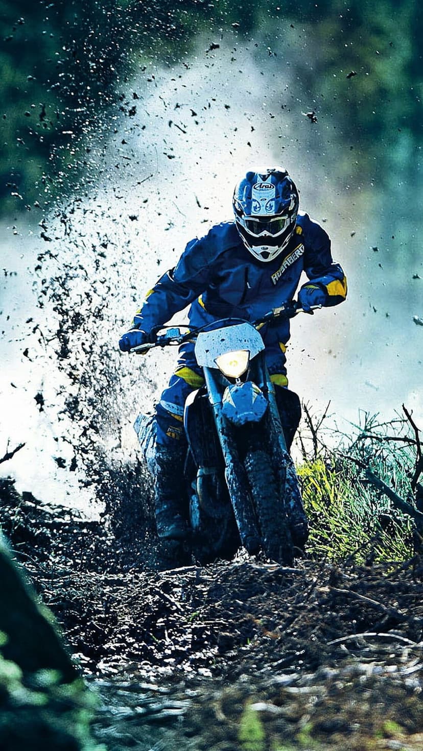 Motocross rider in blue and yellow gear leans into a turn as wet mud and debris spray from the spinning tires.