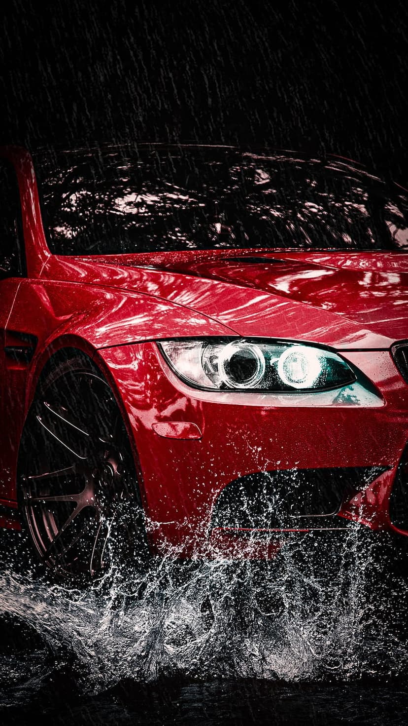 Red sports car splashes through deep puddles during a rainstorm with water spray flying off the front wheels.
