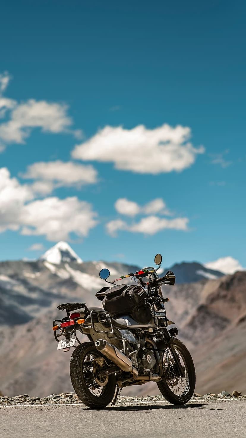 Adventure motorcycle with luggage parked on a rocky roadside facing massive snow-capped mountains under a blue sky.