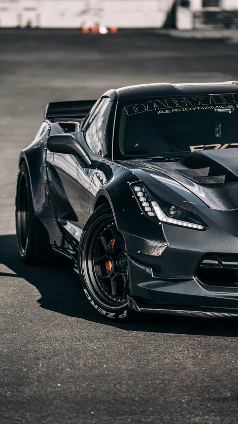 Black widebody Corvette Z06 with P Zero tires and a large rear wing parked on a grey asphalt racing track surface.