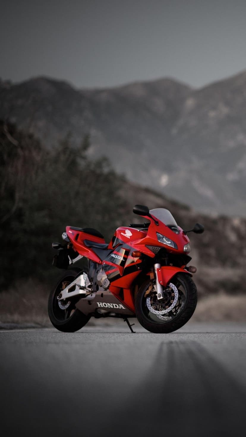 Red Honda CBR sportbike parked on an asphalt mountain road with foggy hills and green trees in the background.