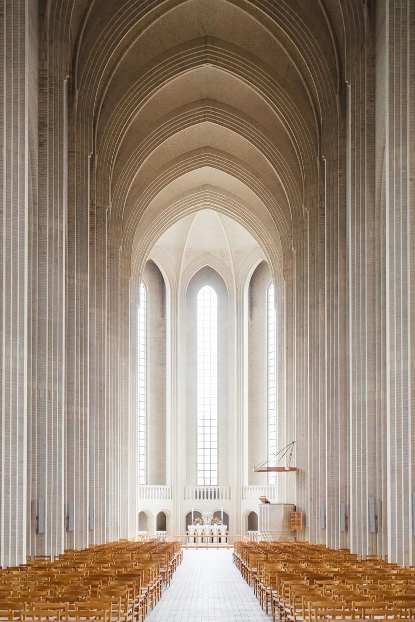 High vaulted ceilings and pointed concrete arches of a minimalist church interior with wooden pews and soft light.