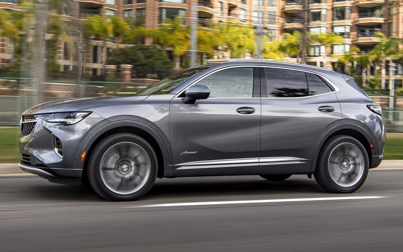 Gray Buick Envision Avenir SUV driving at speed with motion blur against a blurred urban architecture backdrop.