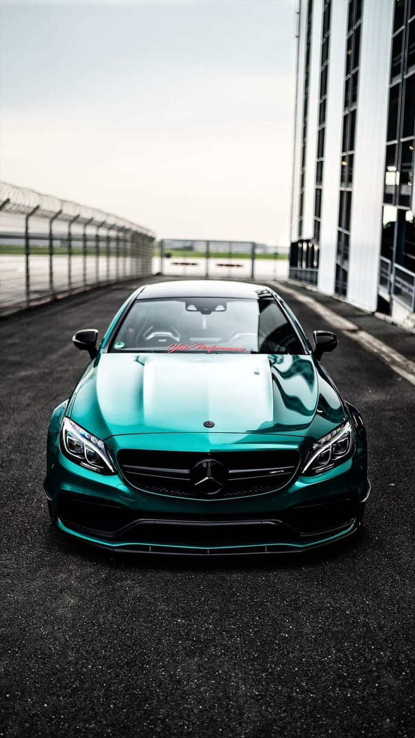 Emerald green Mercedes-AMG C63 parked on a dark asphalt racing track with sharp headlights and a metallic finish.