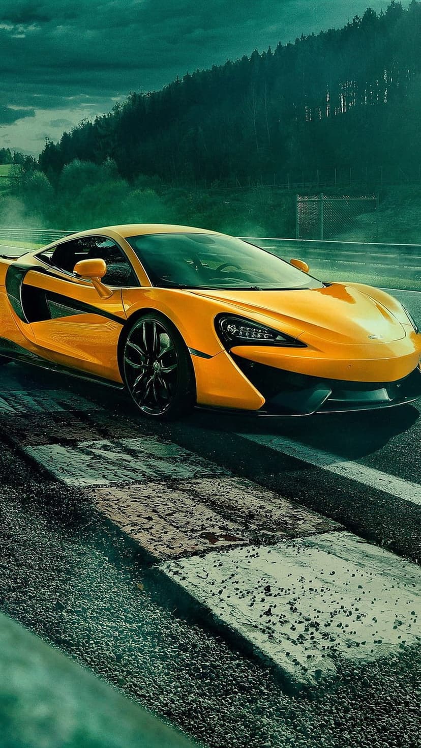 Orange McLaren supercar speeds on a dark racetrack under stormy skies with green forests in the background.