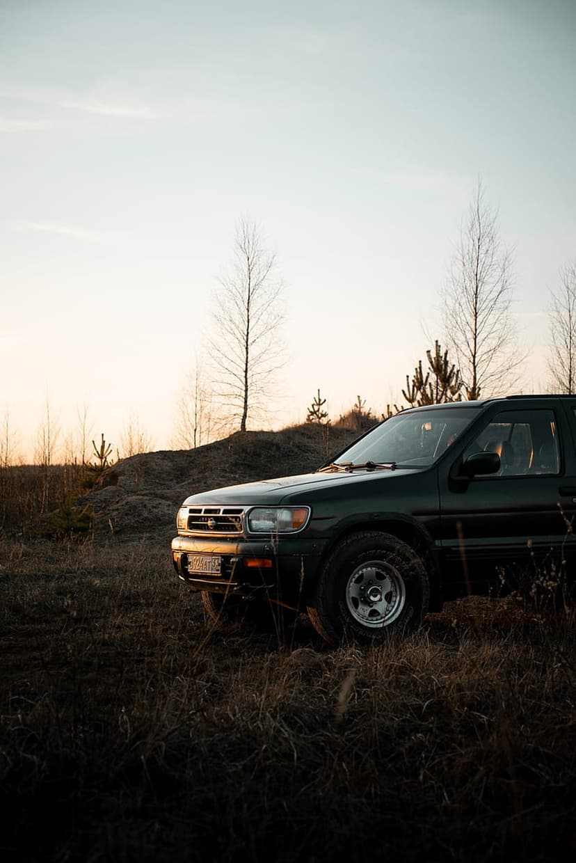 Dark SUV with rugged tires parked in a field of dry yellow grass during a warm orange and blue sunset.