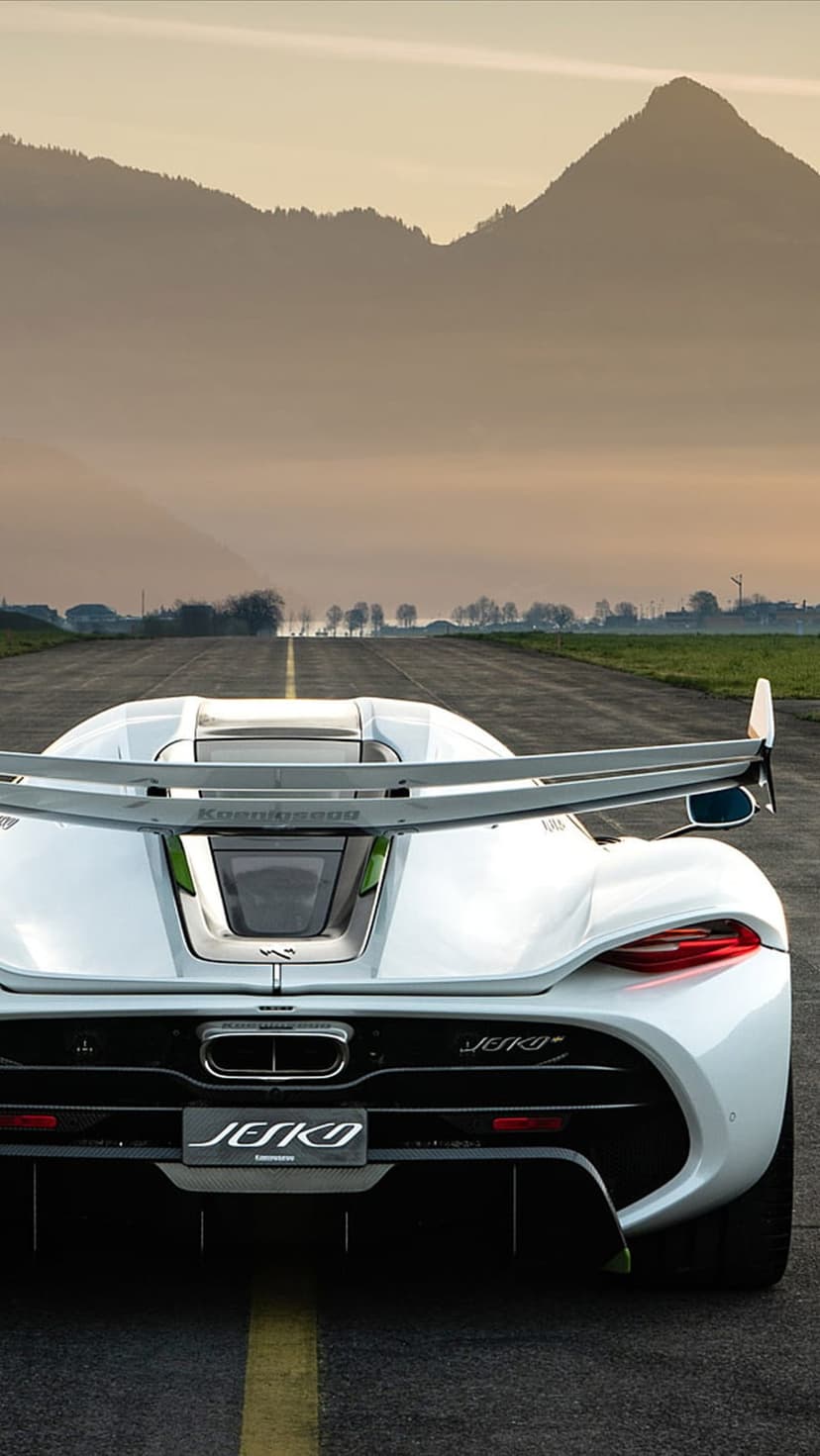 Koenigsegg Jesko rear wing and taillights on a runway with distant mountains during a golden hour sunset.