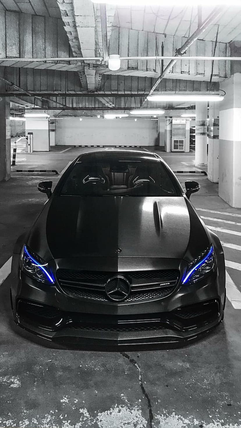 Mercedes-Benz AMG with glowing blue LED headlights parked inside a concrete garage with a dark metallic finish.