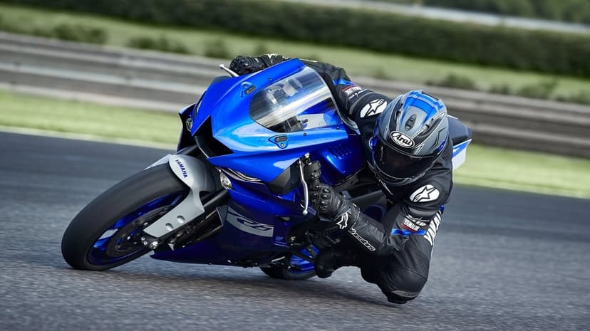 Professional rider on a blue Yamaha sportbike leaning deep into a turn on a paved racetrack at high speed.