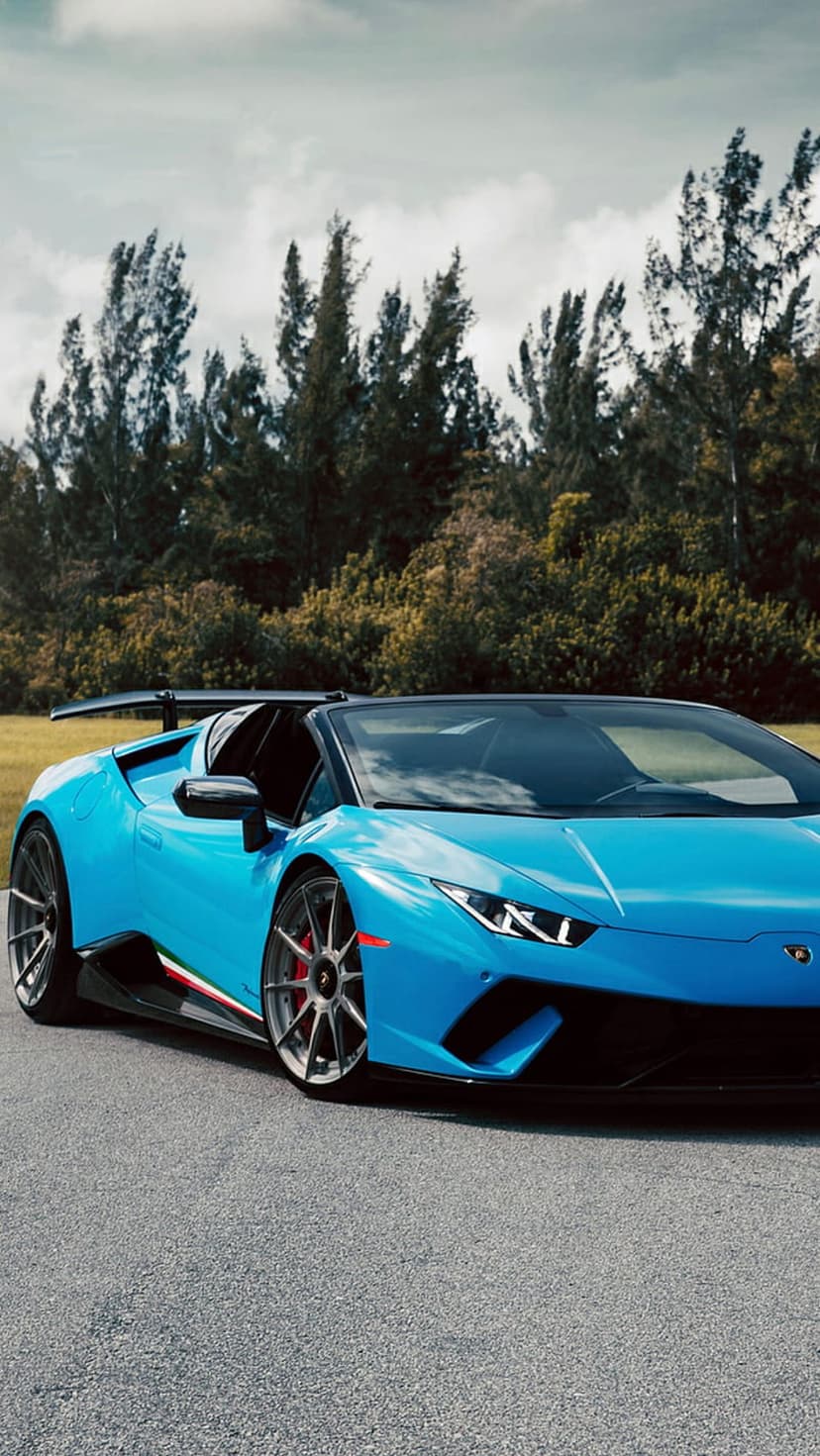 Blue Lamborghini Huracan Spyder with its top down parked on a forest road under a cloudy, grey sky.