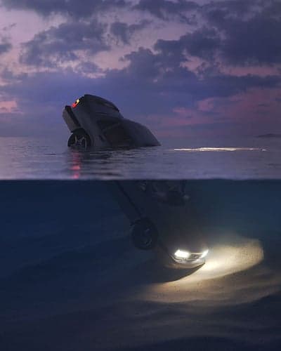 Car submerged in ocean at dusk with headlights on
