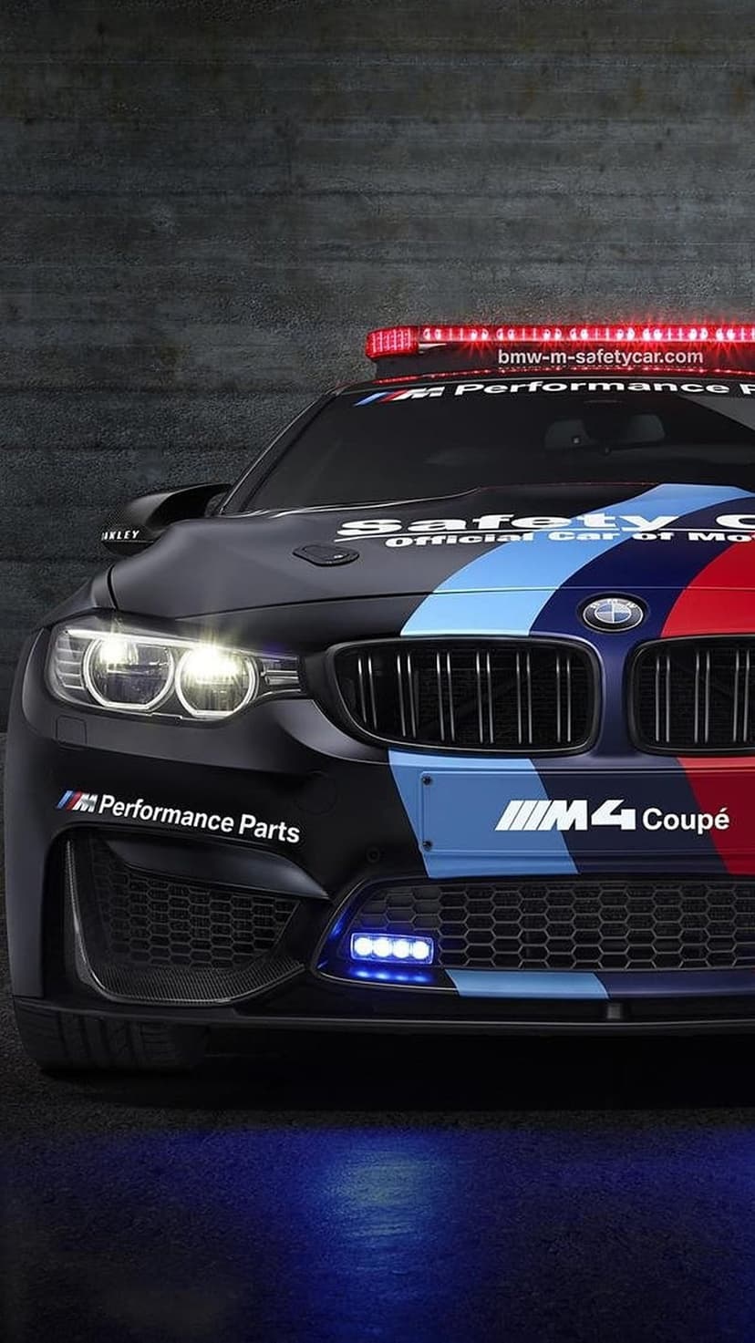 BMW M4 safety car with a red LED roof light and racing stripes parked against a dark gray background.
