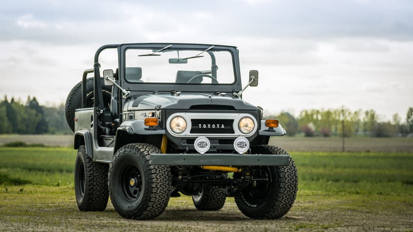 Dark grey Toyota Land Cruiser FJ40 off-road vehicle with large tires in a green field under a cloudy sky.