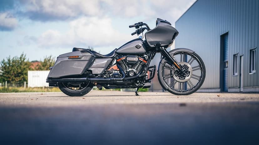 Grey custom bagger motorcycle with a large front wheel parked in front of a modern metal building.