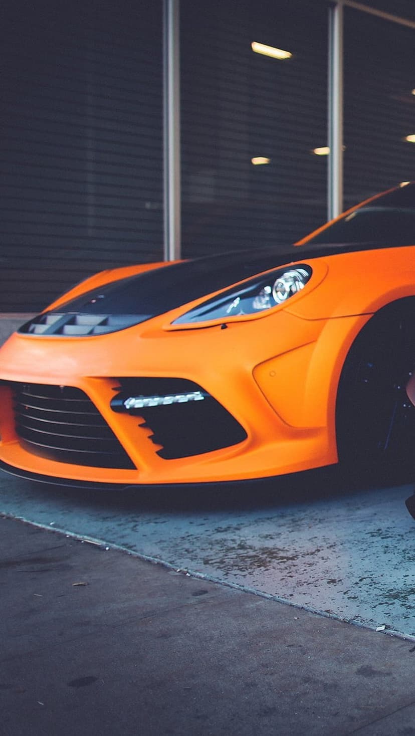 Orange Porsche Panamera with widebody kit, matte black hood, and LED headlights viewed from the front.