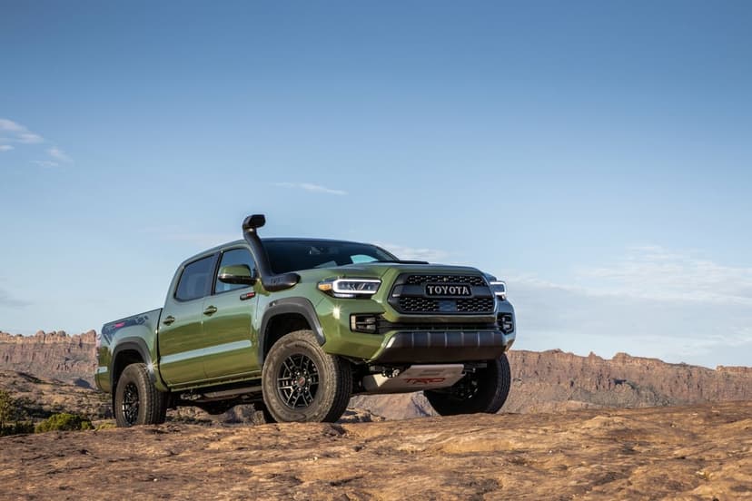 Army green Toyota Tacoma TRD Pro truck on a rocky desert peak under a clear blue sky with bright sunlight.
