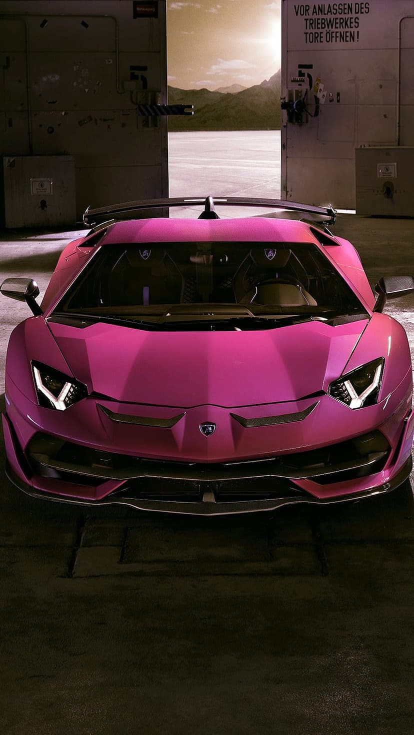 Pink Lamborghini Aventador SVJ with illuminated headlights parked in a dark garage showing sharp front-end details.