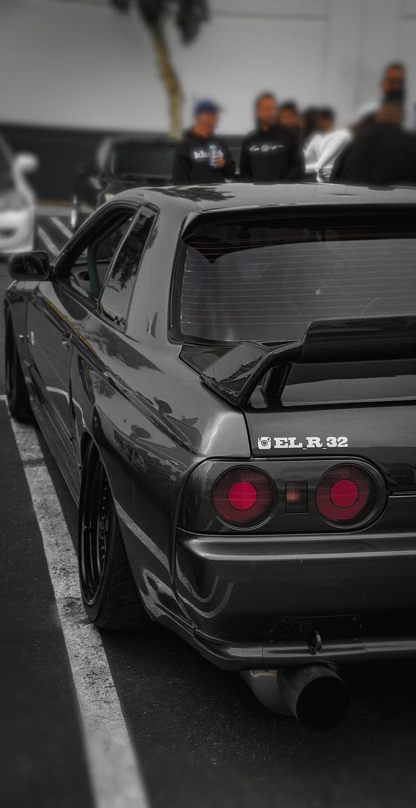 Nissan Skyline R32 GT-R rear view with round red taillights and a large wing at a night car meet.