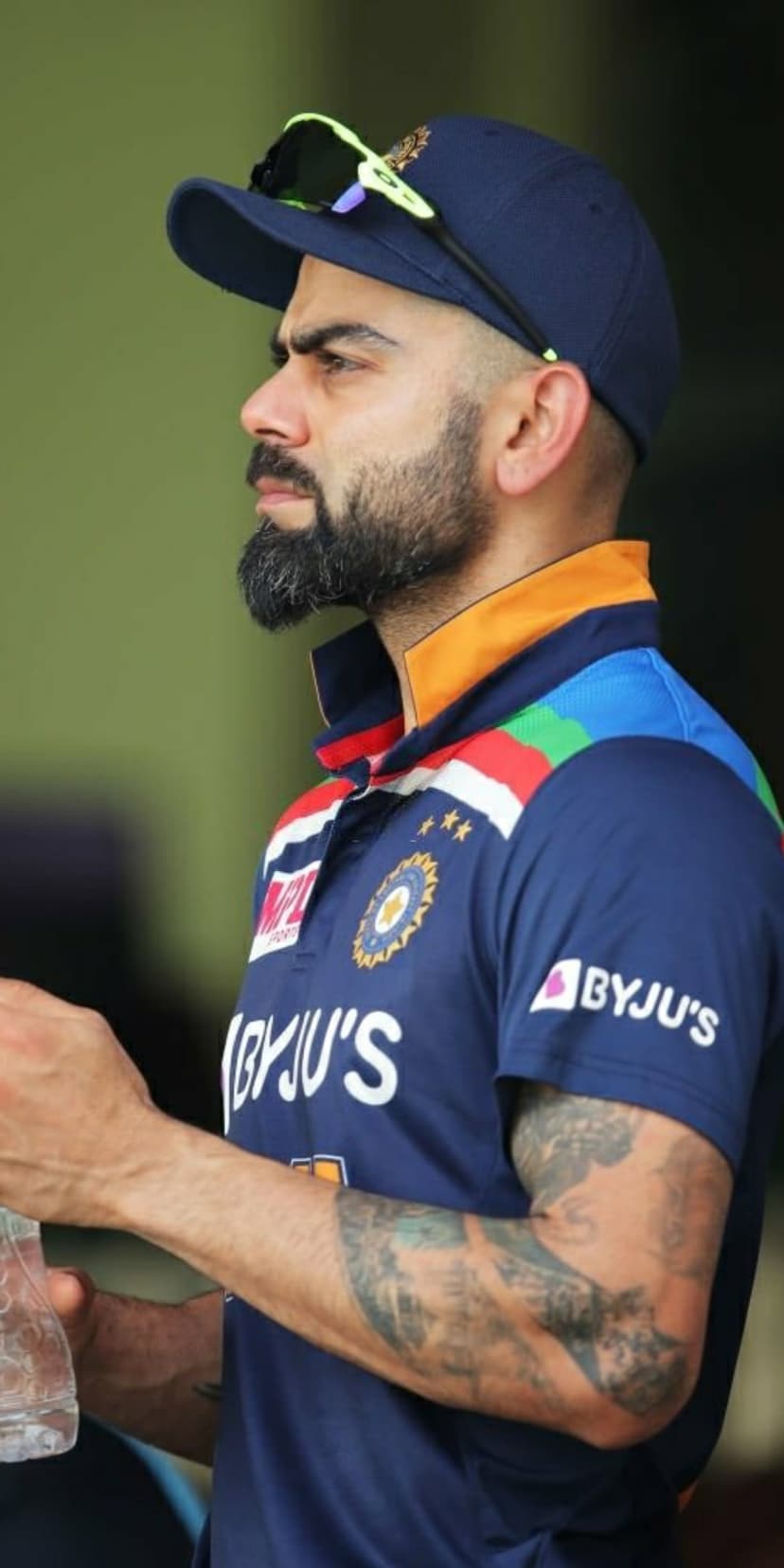 Virat Kohli wearing a blue Indian cricket jersey and cap with sunglasses while looking aside in profile view.