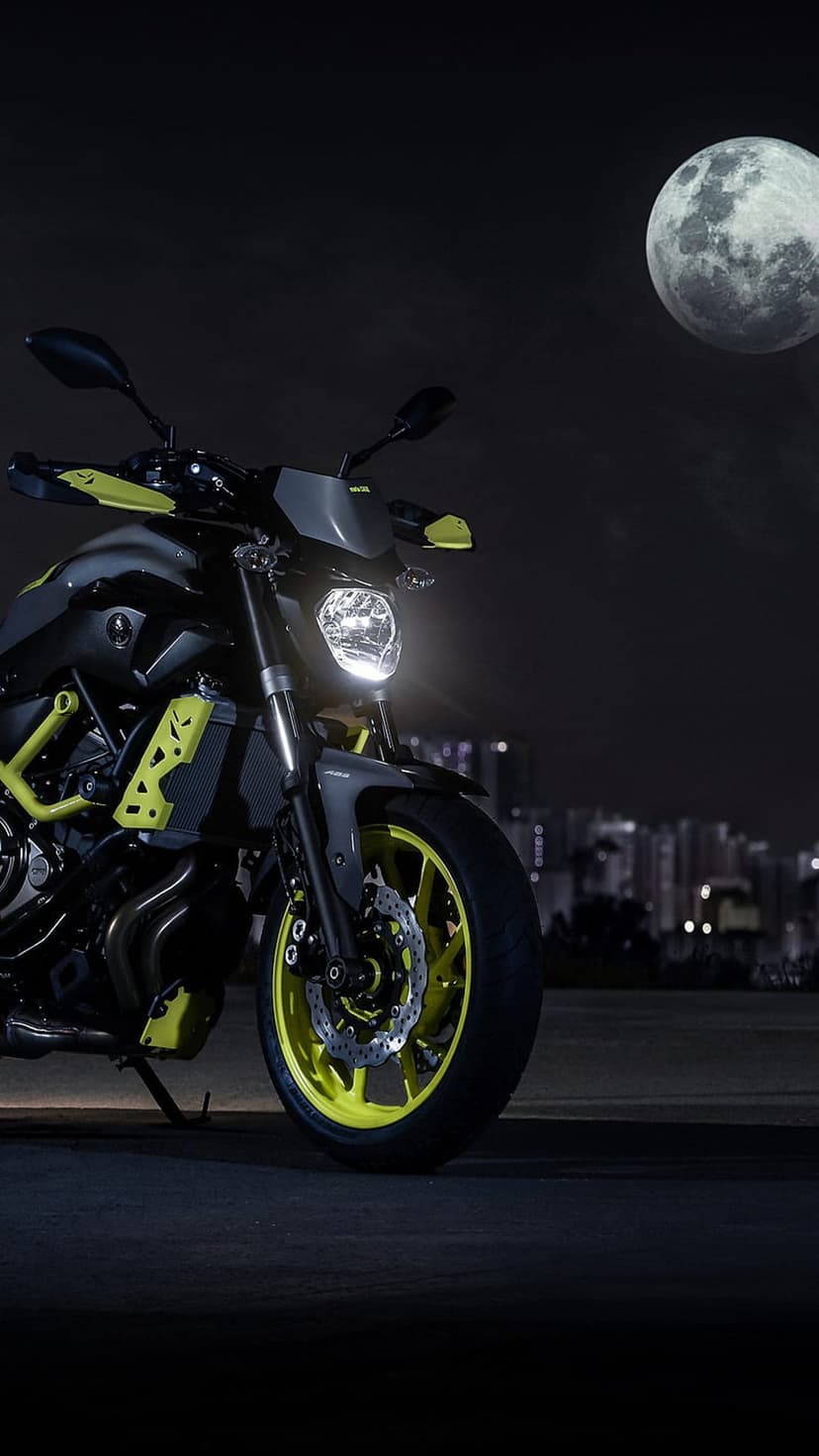 Yamaha motorcycle with yellow trim parked on a dark road under a full moon and glowing city skyline at night.