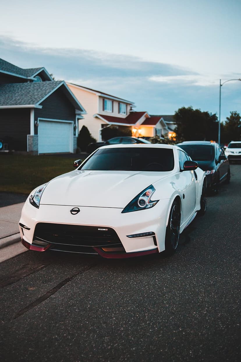 White Nissan 370Z Nismo with red trim parked on a suburban road under a dusky twilight sky during evening.
