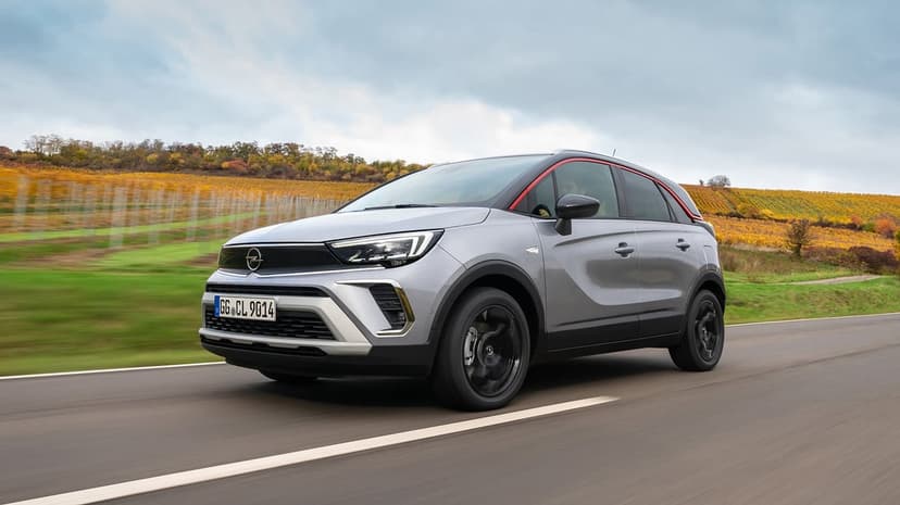 Silver Opel Crossland SUV driving on a paved road past yellow autumn vineyards under a dramatic overcast sky.
