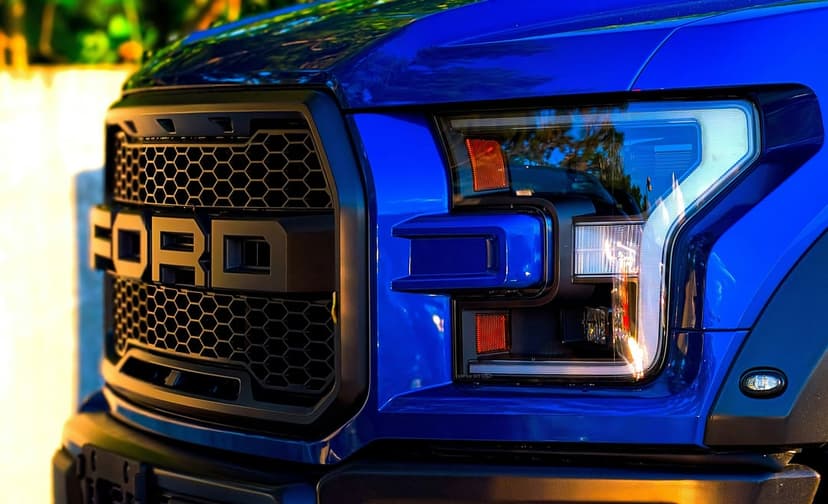 Blue Ford Raptor truck grille with bold lettering and a modern LED headlight assembly in a detailed close-up.