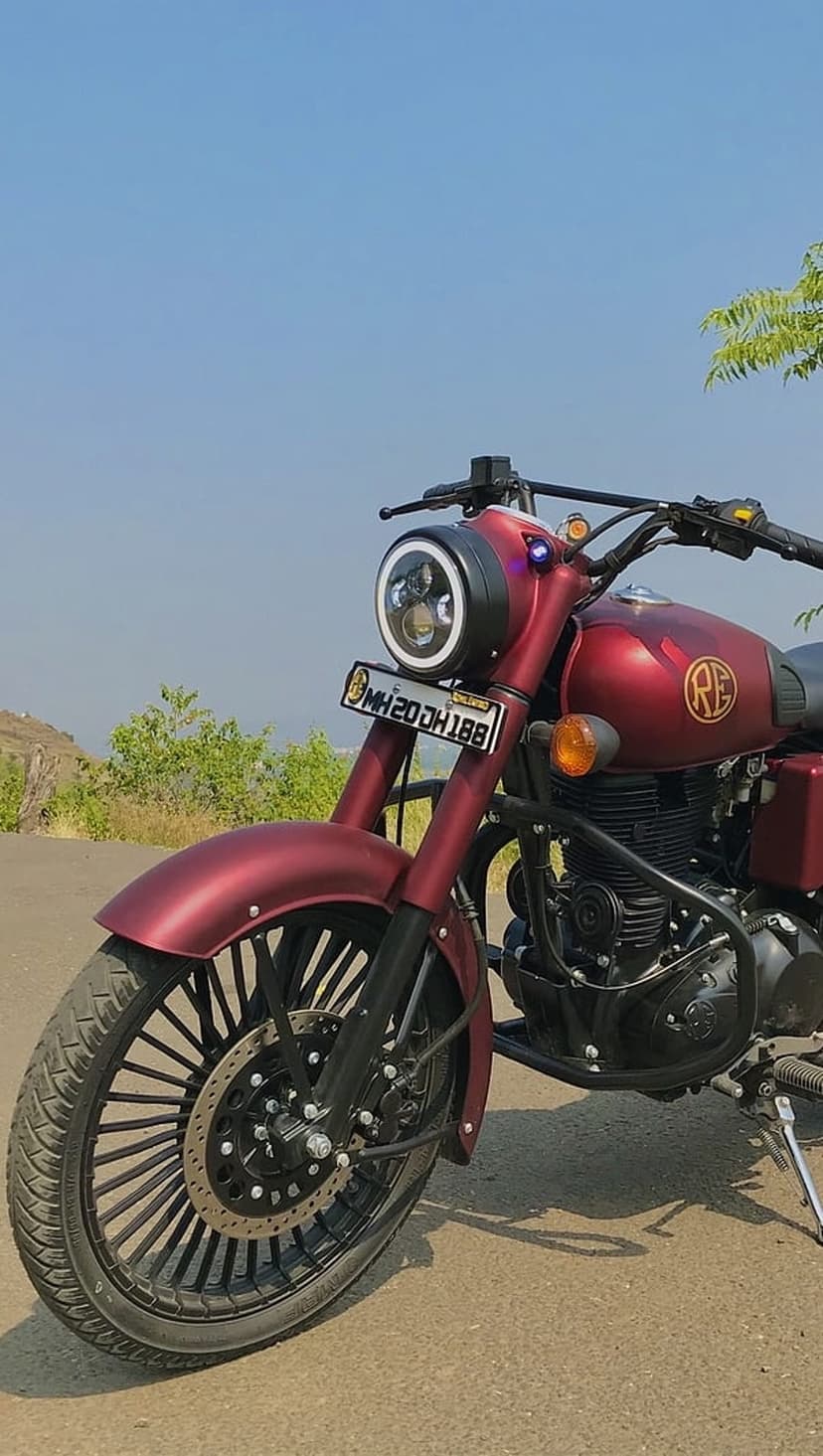 Maroon Royal Enfield motorcycle with a circular LED headlight and custom spoke wheels parked on a paved road.