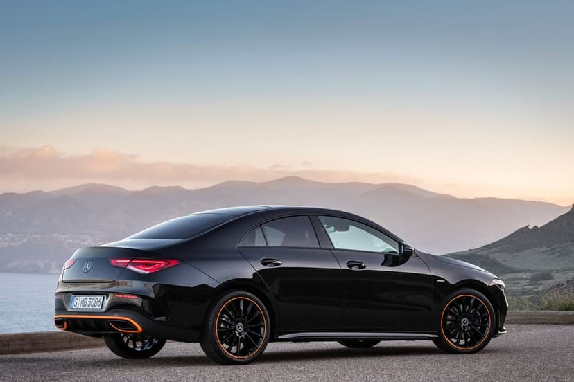 Black Mercedes-Benz CLA coupe with orange wheel accents parked on a roadside overlooking misty sunset mountains.
