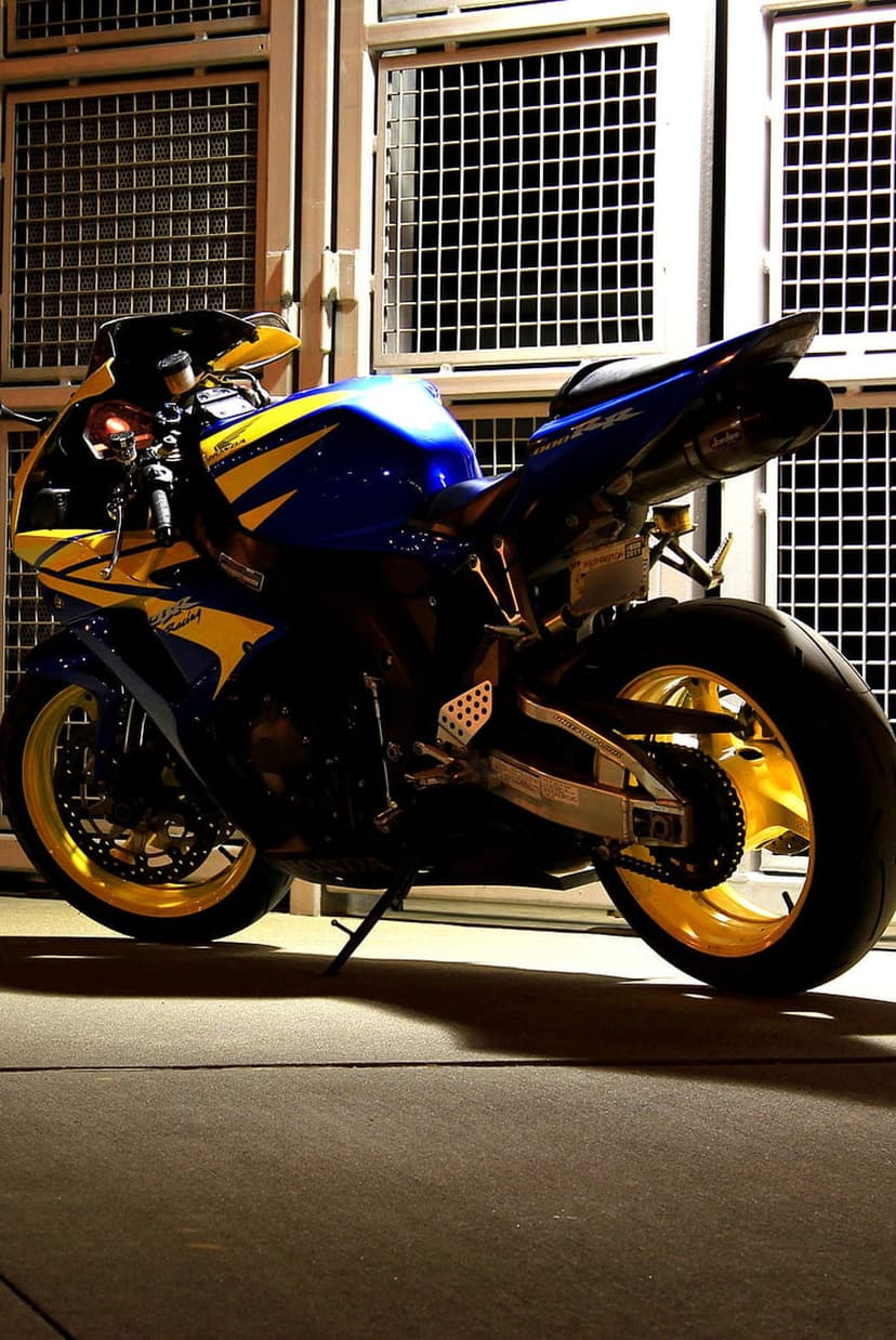 Blue and yellow sportbike with gold wheels parked in front of a gray grid wall with dramatic shadows and lighting.