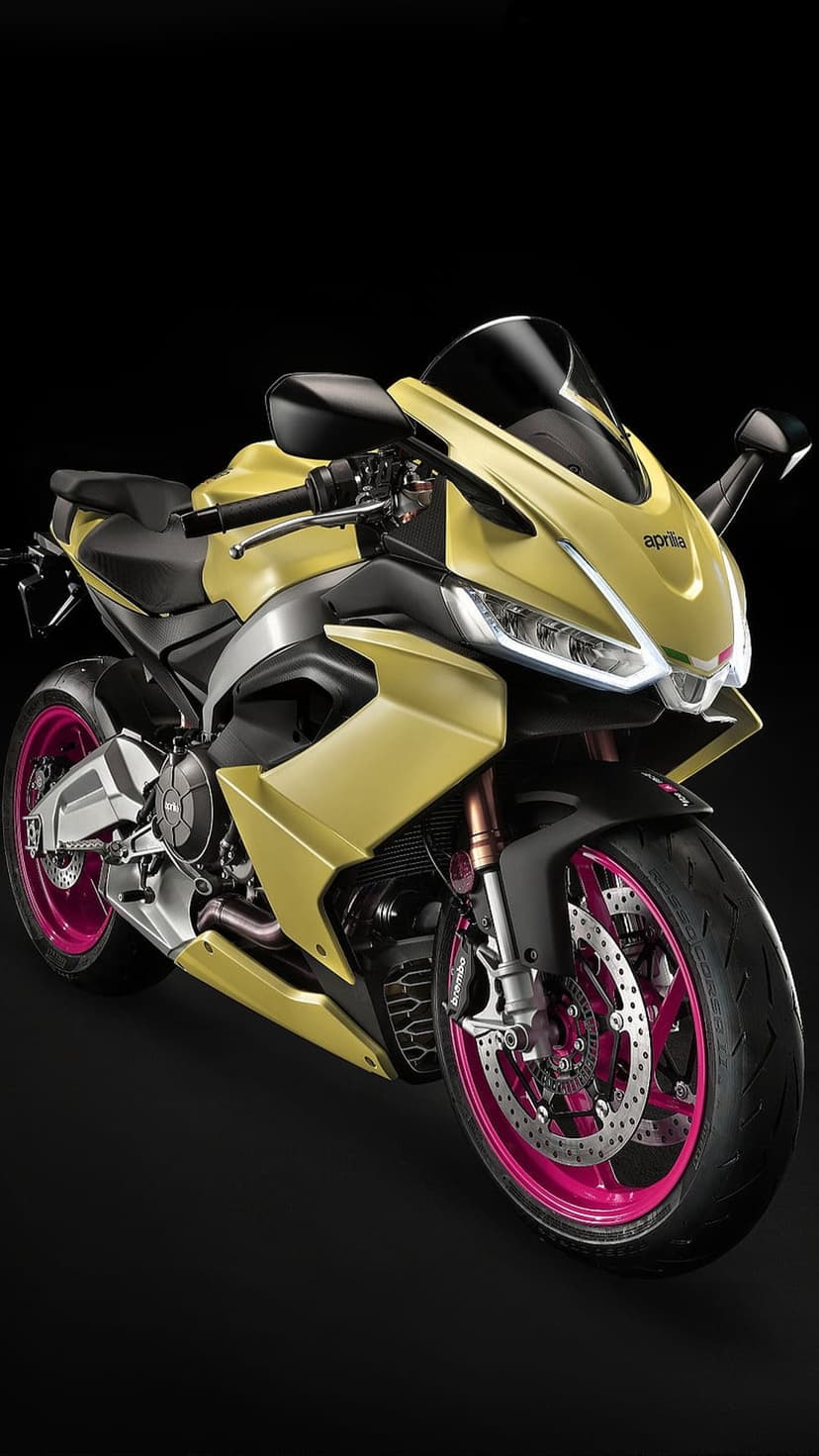 Yellow Aprilia sportbike with neon pink wheels and gold accents set against a solid dark black background.