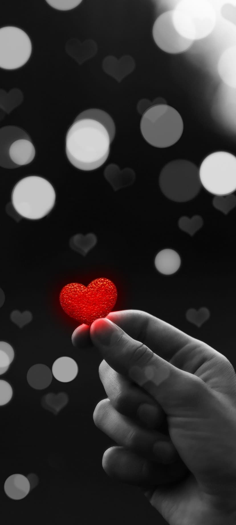 Hand cradling a textured glowing red heart surrounded by soft heart-shaped bokeh on a dark background.