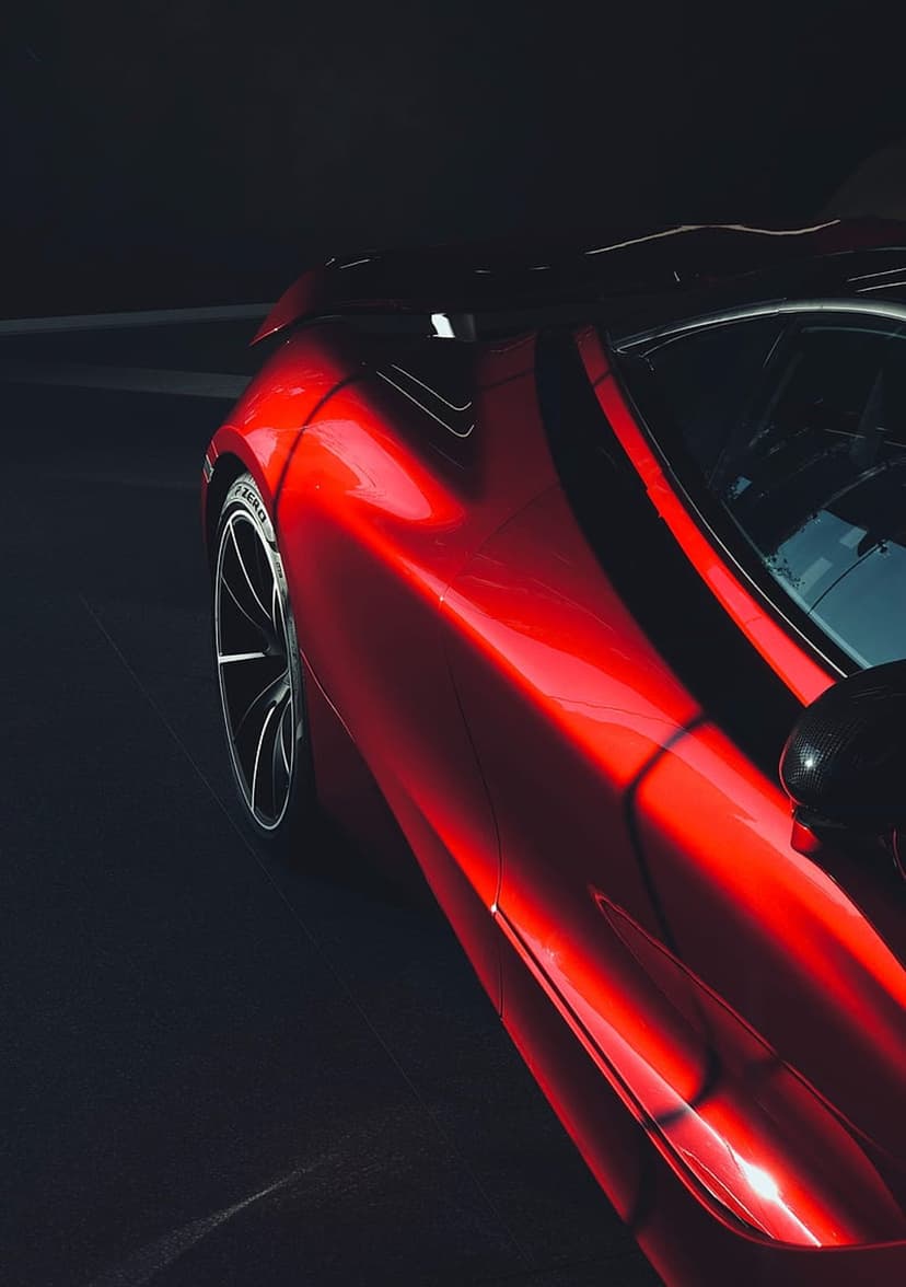 Crimson sports car with glossy red paint, reflective bodywork, and detailed alloy wheel in dramatic low lighting.