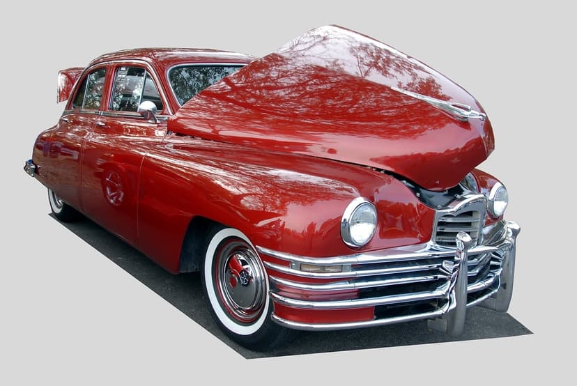 Vintage red Packard sedan with an open hood, chrome grille, engine components, and classic whitewall tires.