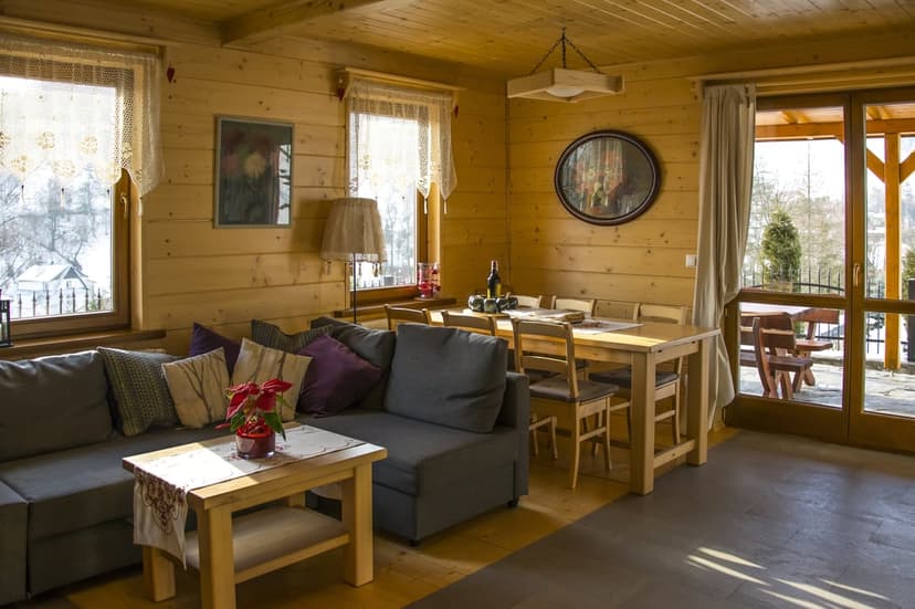 Wooden cabin interior featuring a gray sectional sofa, round mirror, and dining table under warm indoor lighting.