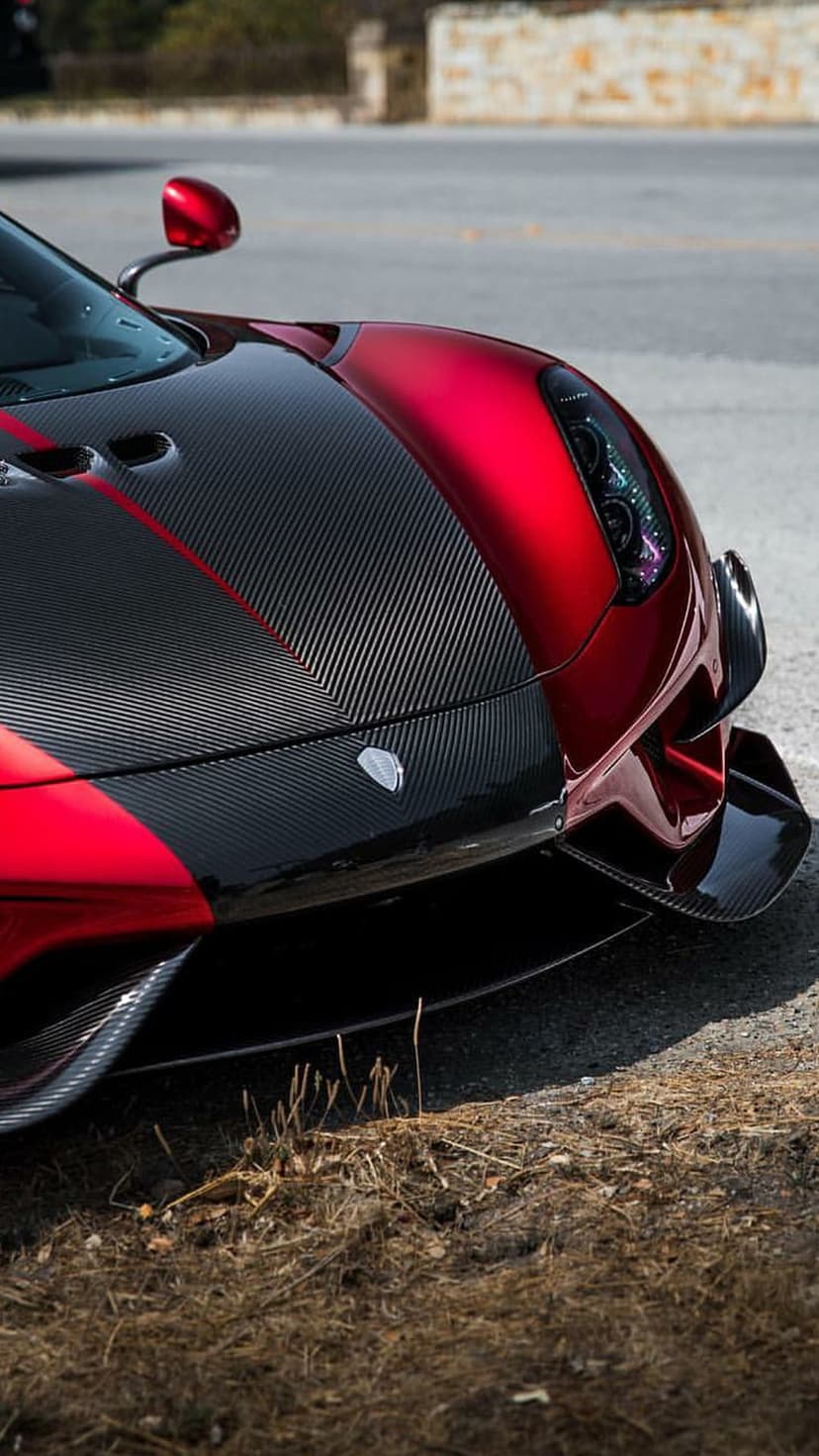 Red sports car hood features a glossy finish and dark carbon fiber weave texture on an aerodynamic front panel.