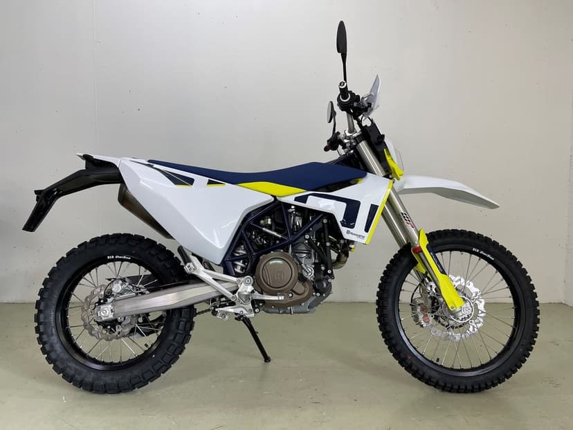 Side profile of a white Husqvarna 701 Enduro motorcycle with blue and yellow accents in a clean studio space.