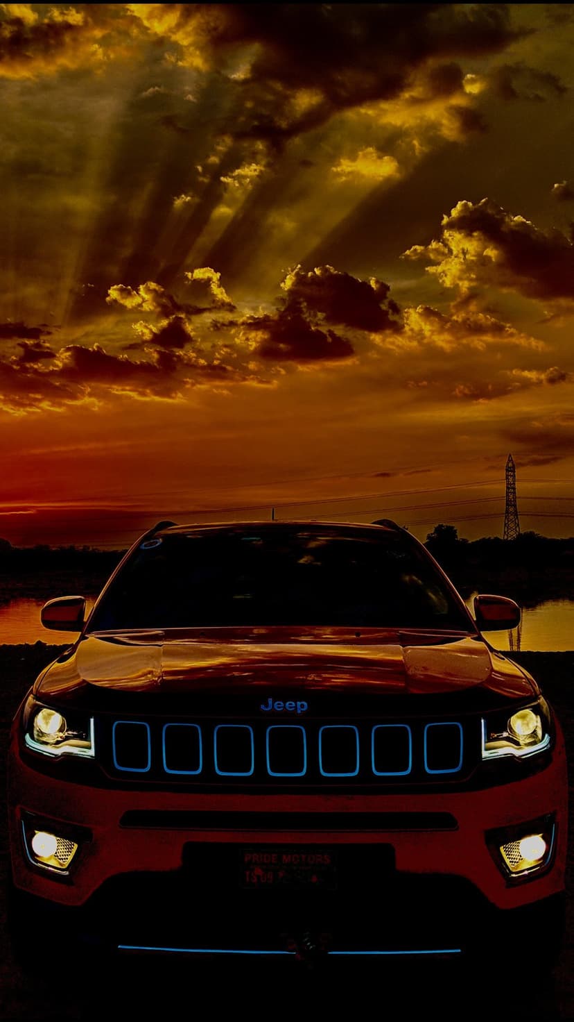Jeep SUV front view at sunset with golden god rays, blue-lit grille accents, and glowing headlights.