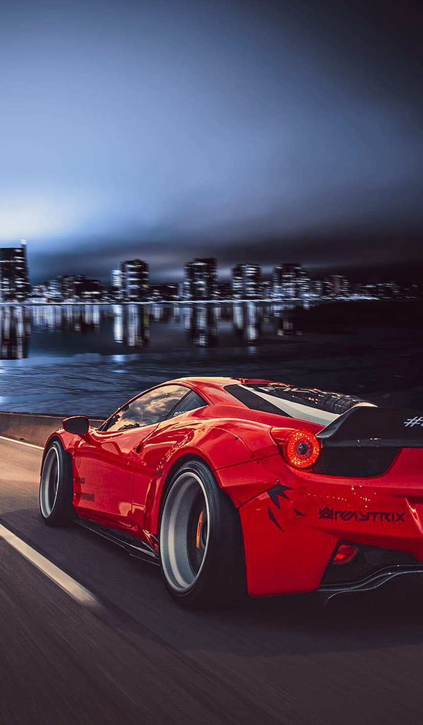 Red Ferrari sports car speeding on an urban highway at night with blurred city lights and water reflections.