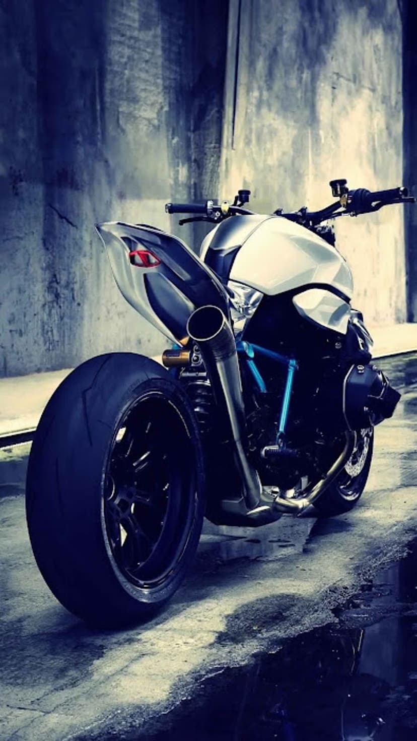 White motorcycle rear tire and polished chrome exhaust pipe resting on a textured concrete urban street.