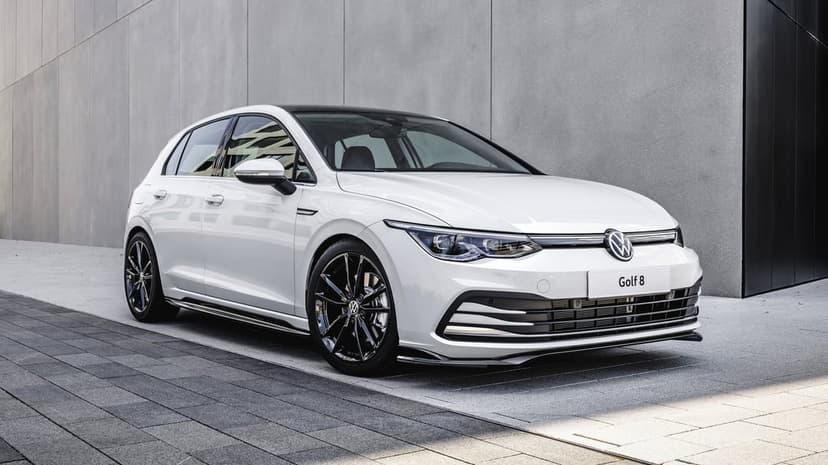 White Volkswagen Golf 8 with black wheels parked against a modern grey concrete wall in natural daylight.