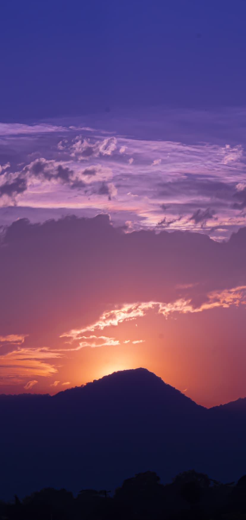 Jagged mountain peak silhouetted against a vibrant purple and orange twilight sky with scattered soft cloud wisps.