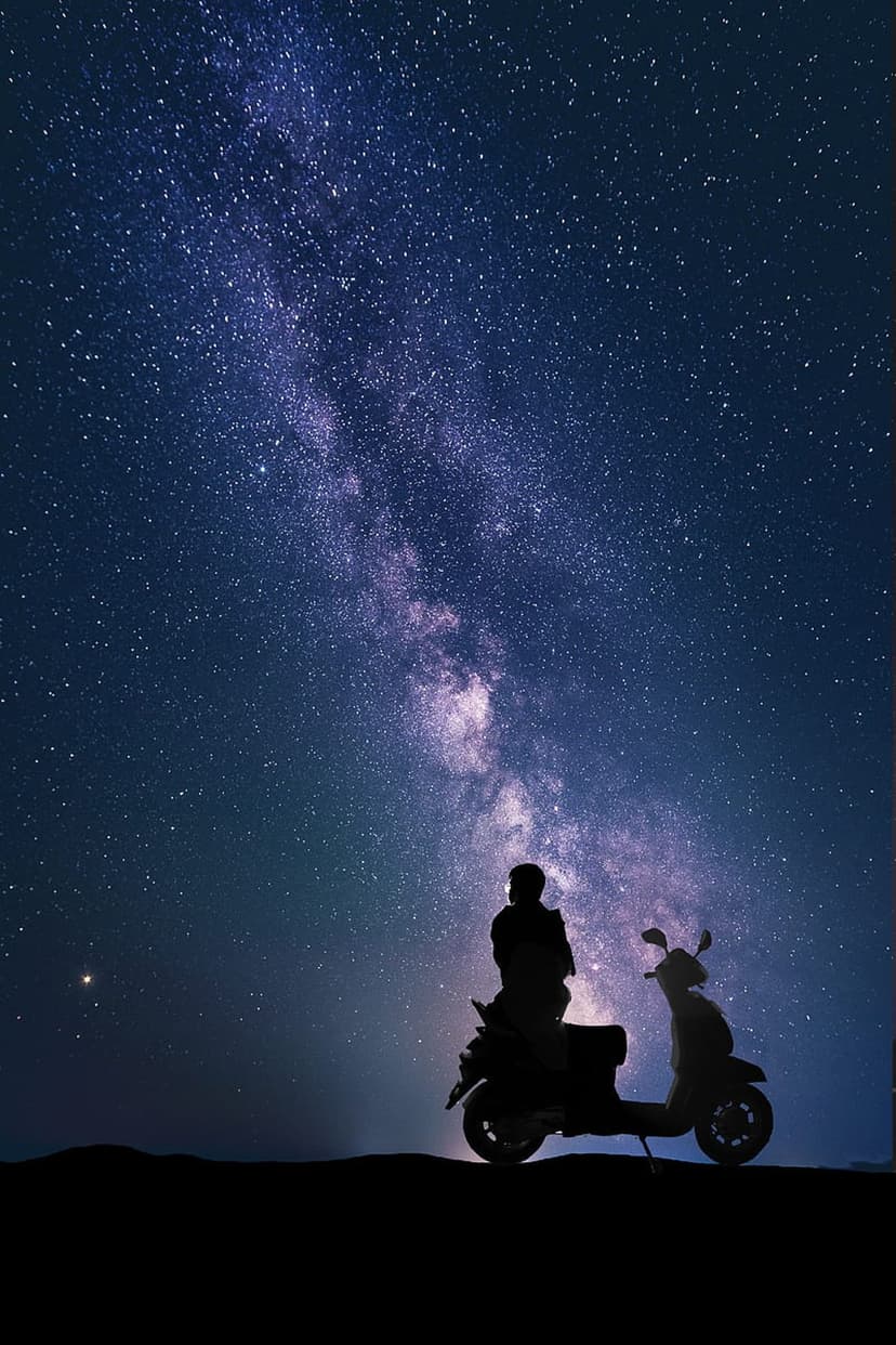 Person on a scooter silhouetted against a brilliant Milky Way galaxy and a star-filled night sky on a hill.
