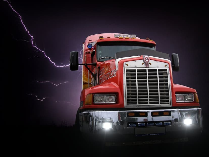 Red Kenworth semi-truck with chrome grille parked under a dark purple sky filled with lightning bolts.
