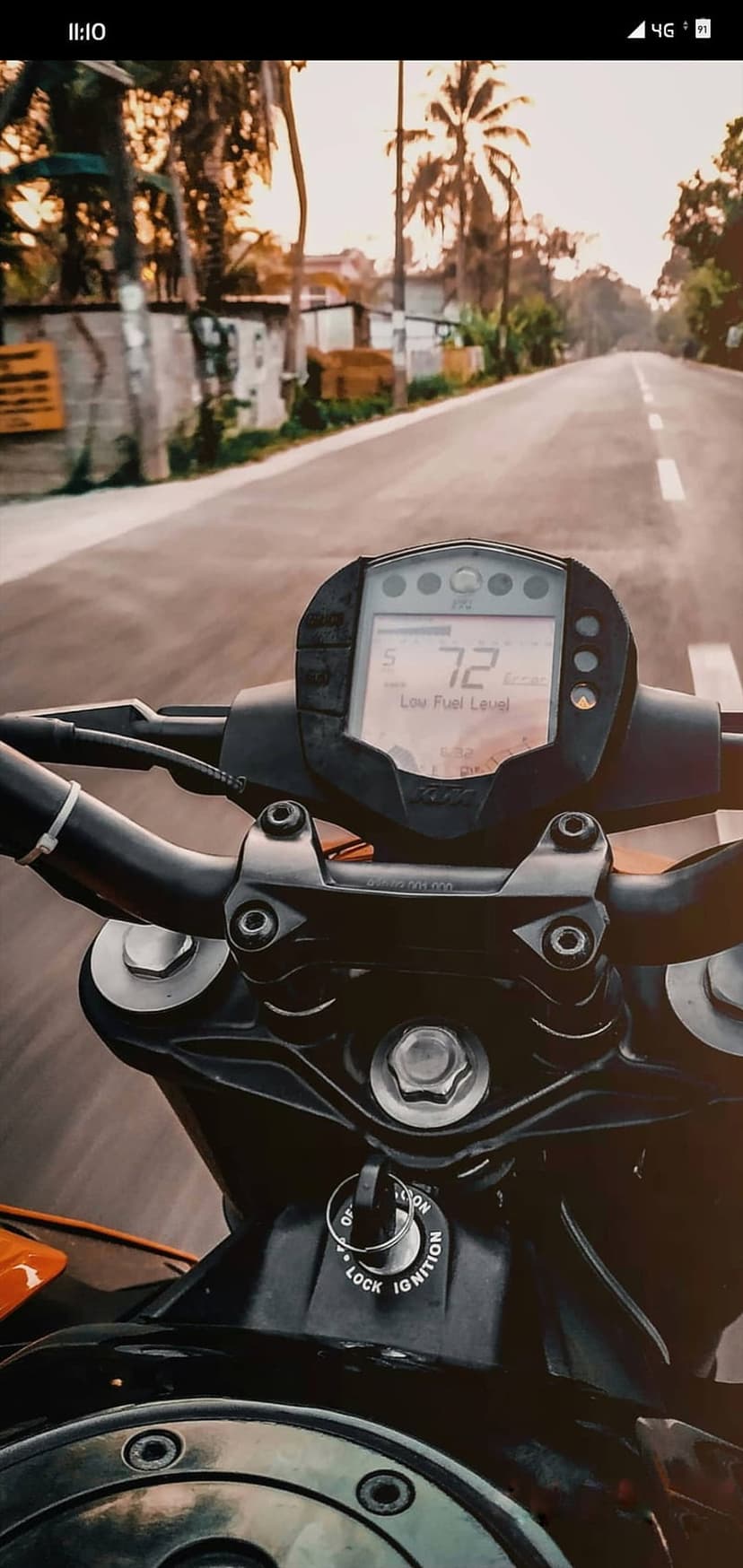 Motorcycle dashboard showing speed and low fuel on a scenic road with palm trees under a warm sunset sky.
