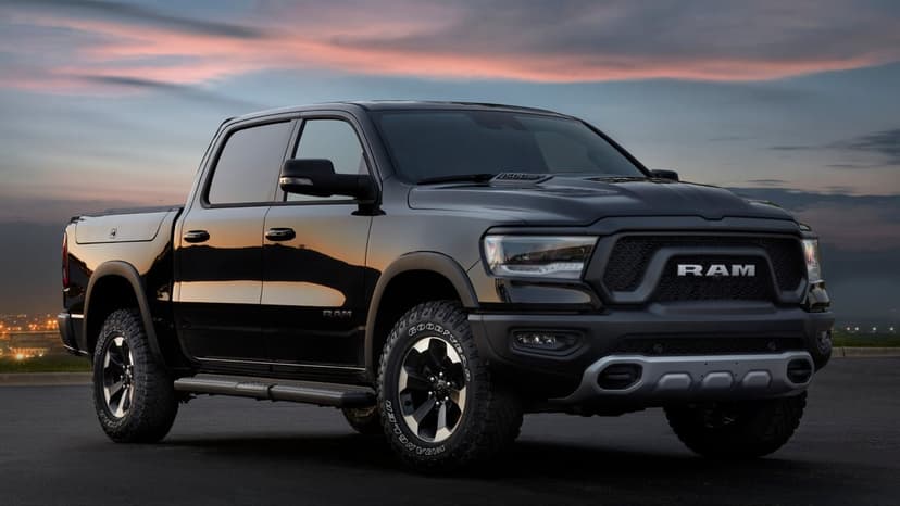Black Ram 1500 Rebel truck on asphalt with a pink and blue sunset sky reflecting on its body.